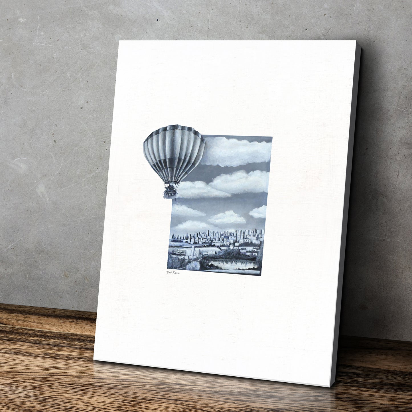 Print a realistic drawing. In the center there is a landscape rectangle, with mountains and a lake and clouds, from the image a hot air balloon emerges onto the white background surrounding the painting. Vintage photo. A combination of retro and modern design. The painting is placed on a wooden floor, leaning against a gray wall