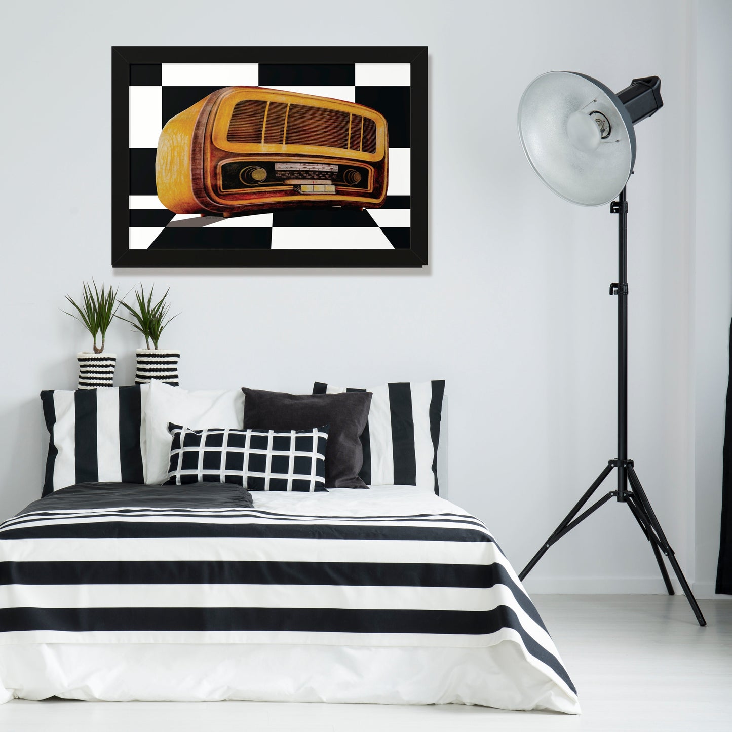 An impressive drawing of an antique radio in the style of the 1970s     
 Black frame, hanging in a youth room in black and white colors. With a double bed with black and white striped bedding. With pots and a black standing lamp